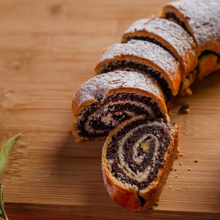 Szeletelt mákos bejgli porcukorral, fa vágódeszkán